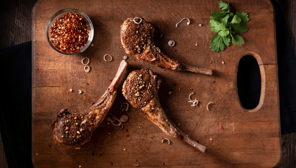 Perfekt gewürzte und gegrillte Lammkoteletts mit Kräutern und Gewürzen auf einem Holzbrett – ideal zubereitet nach dem Lammkoteletts Marinieren.